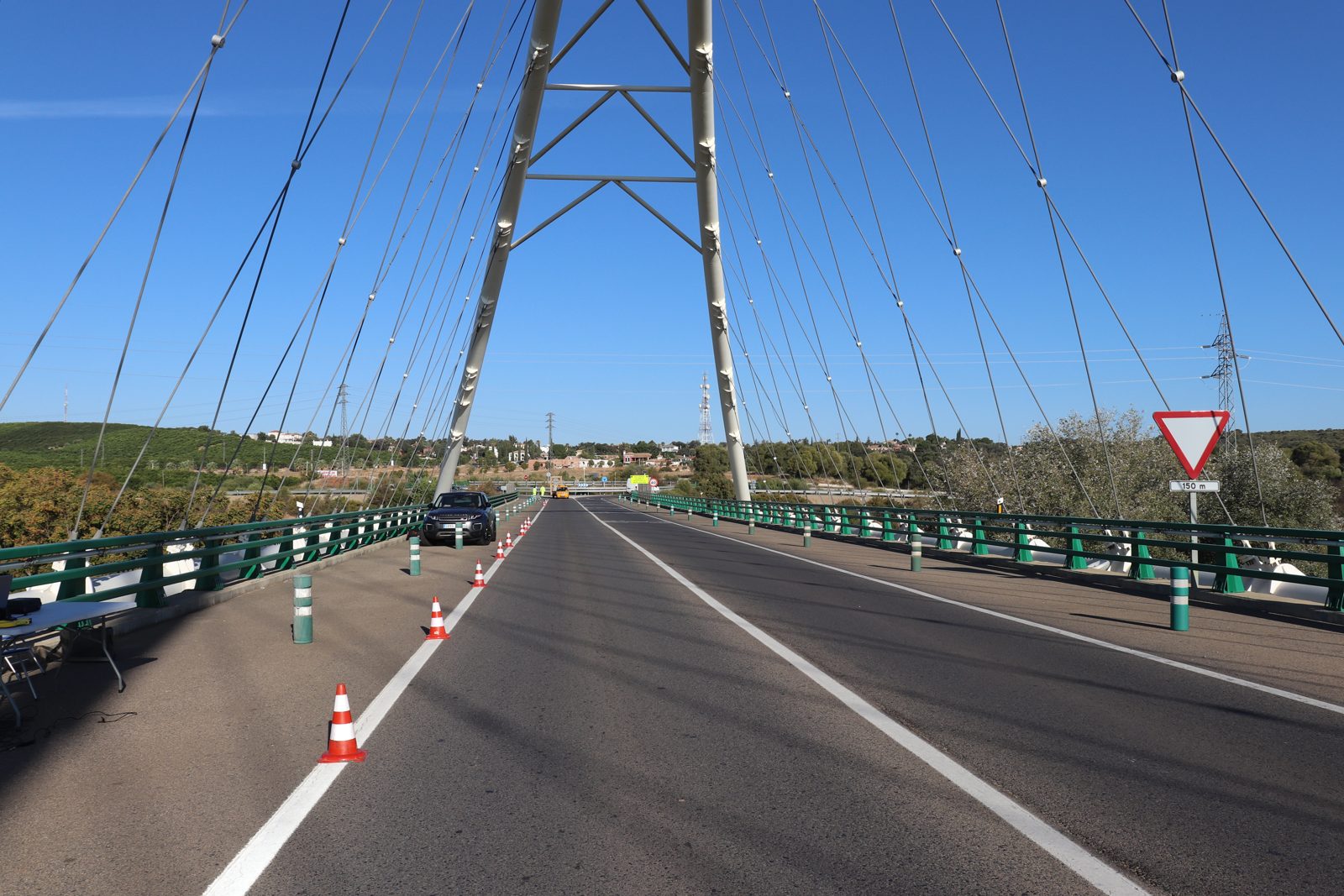 Calzada del puente con conos de señalización y un vehículo, con el arco al fondo